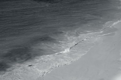 Free Black and white aerial photograph of Albufeira's tranquil beach with gentle waves meeting the shore. Stock Photo