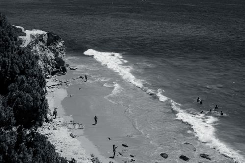 Free Black and white photo capturing Albufeira's scenic rocky shoreline with waves and people enjoying the beach. Stock Photo