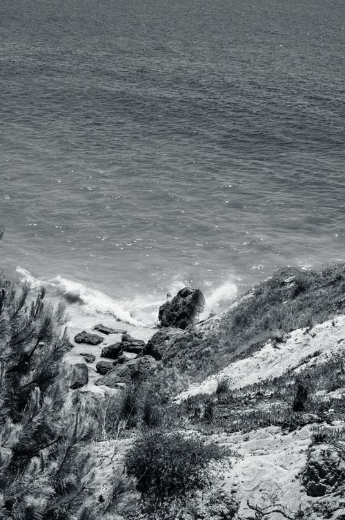 Free Stunning black and white photo of Albufeira's rocky coastline capturing splashing waves against the cliffs. Stock Photo