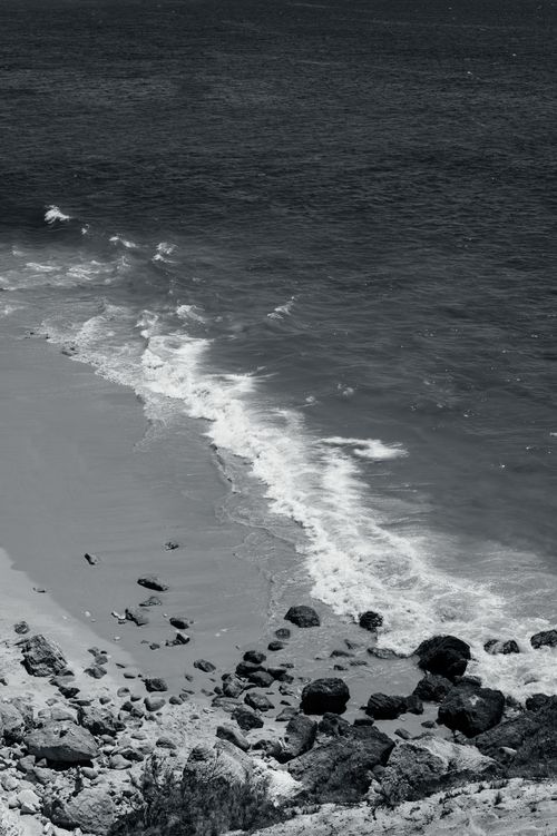 Free A serene black and white shot of Albufeira beach with waves crashing on the rocky shore. Stock Photo