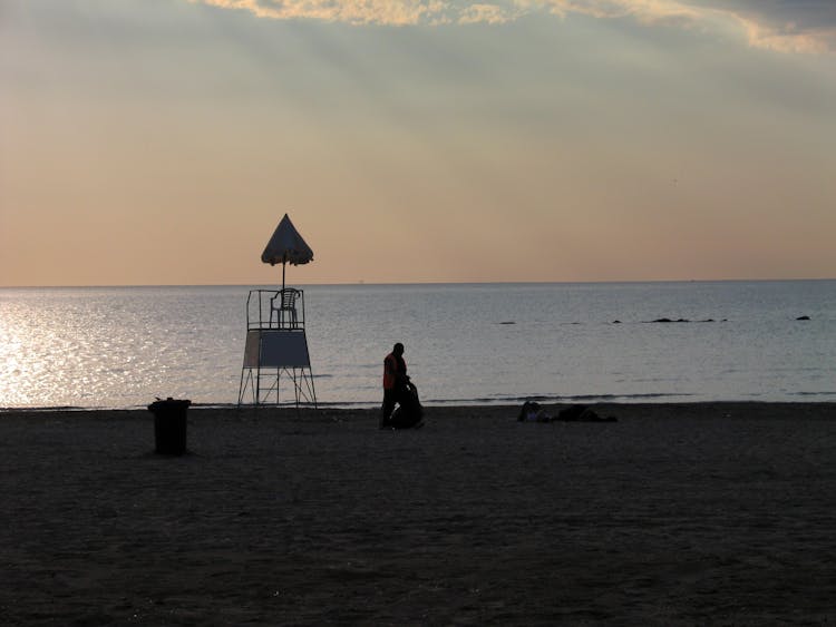 A Man Cleaning The Beach At Sunset 