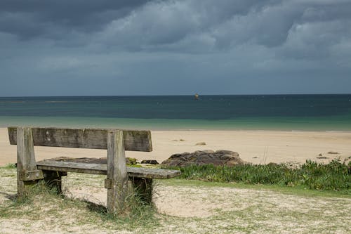 An Empty Wooden Bench Standing on a Beach under a Cloudy Sky 