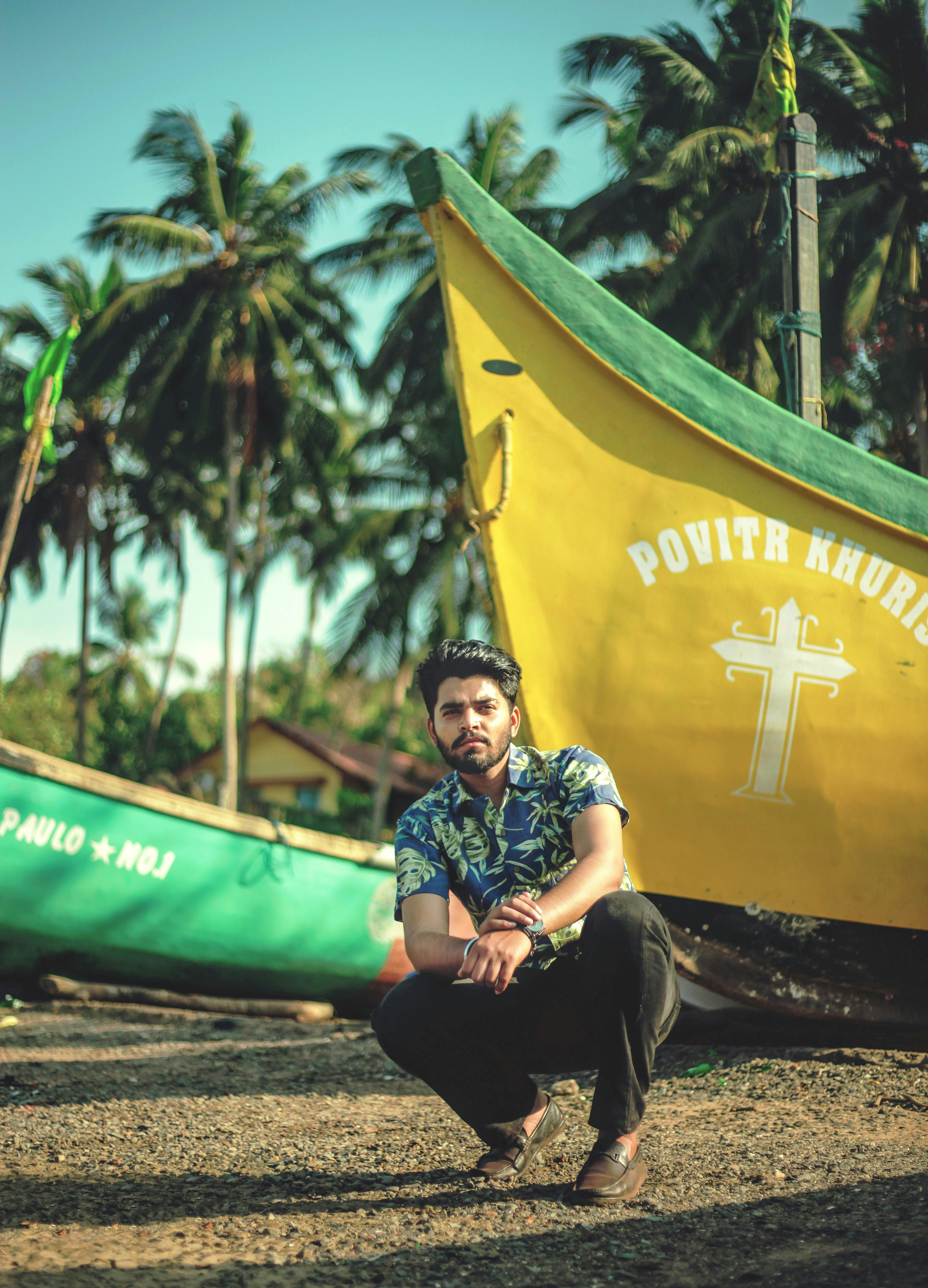 Fashionable man posing beside colorful boats on a sunny beach.