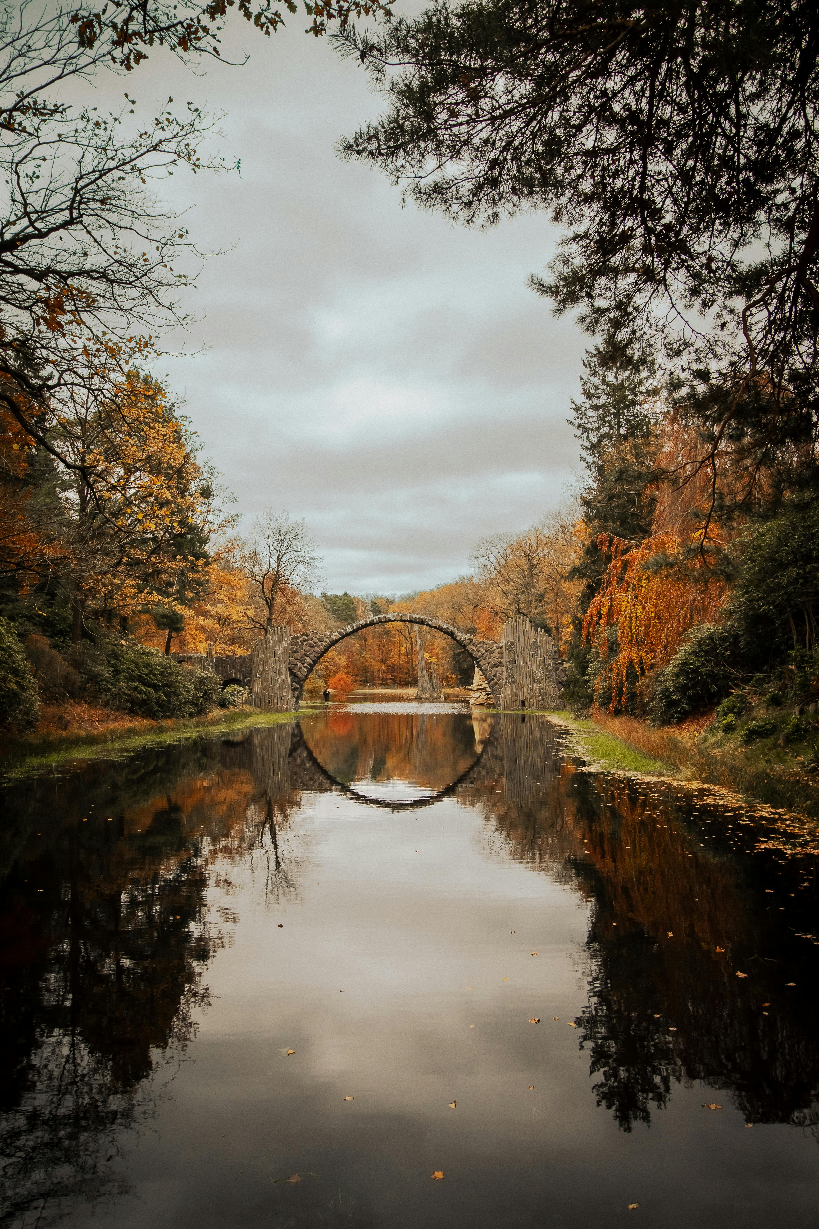 Picturesque view of Rakotzbrücke, an iconic stone bridge in autumn, reflecting on the tranquil river in Gablenz, Germany.