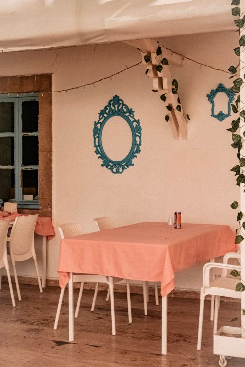 Free Cozy Mediterranean café setup with pink tablecloths, white chairs, and blue decorative accents. Stock Photo