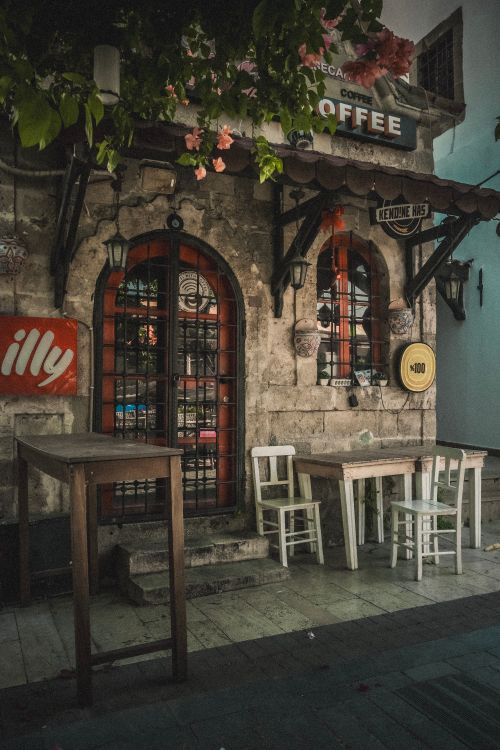 Free Rustic café with vintage charm, showing tables, chairs, and ornate doors, perfect sunlight for an afternoon coffee. Stock Photo