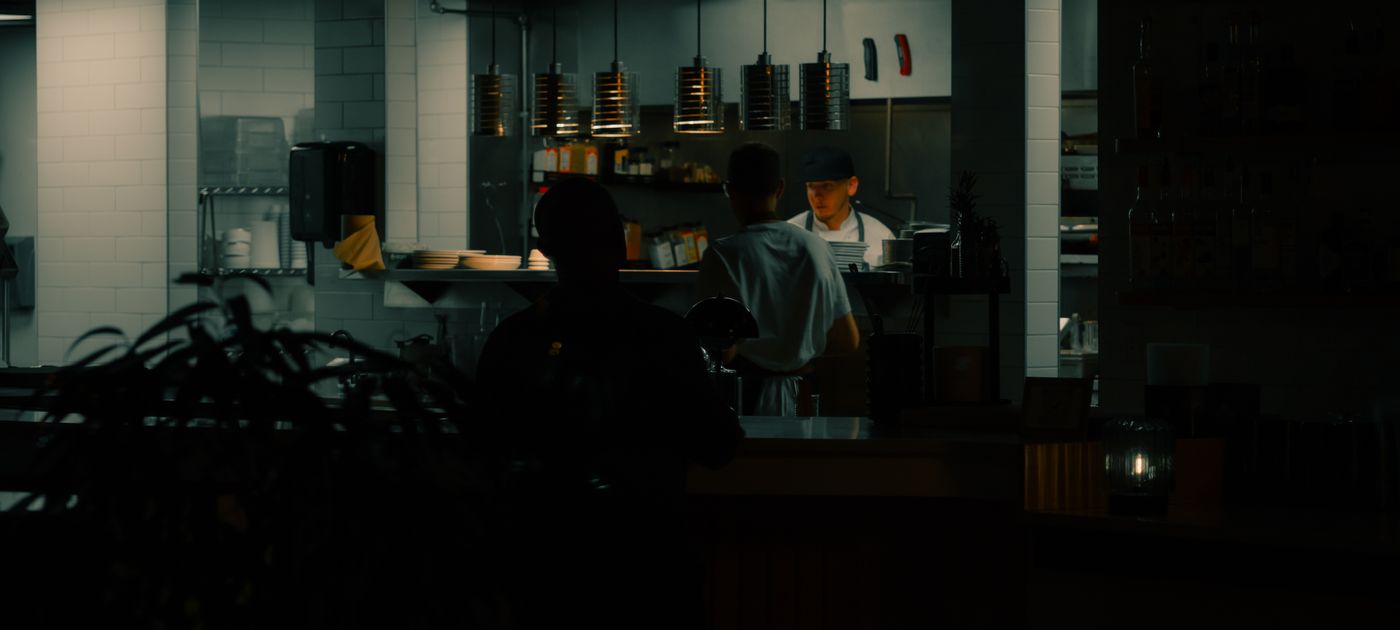 Cooks working a dimly lit late-night restaurant kitchen line — cockroach treatment in a 24-hour mamak happens in the quiet hours