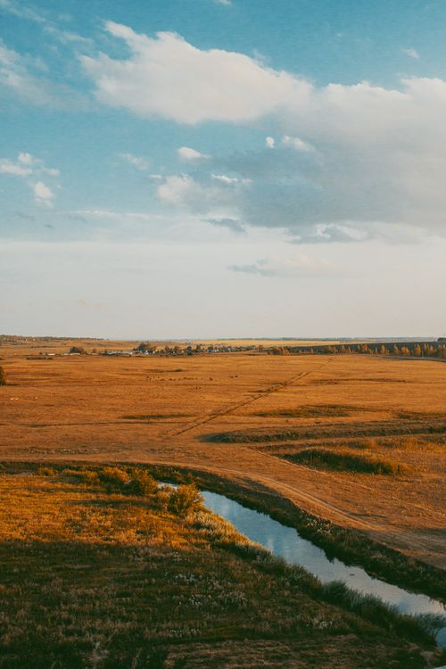 Free Aerial view of an expansive rural landscape with a meandering stream under a clear sky. Stock Photo