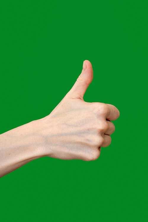 Close-up of a Hand Showing Thumbs Up on Green Background 
