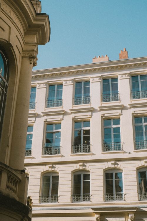 Free A bright street view of a neoclassical residential building's facade with a clear blue sky. Stock Photo