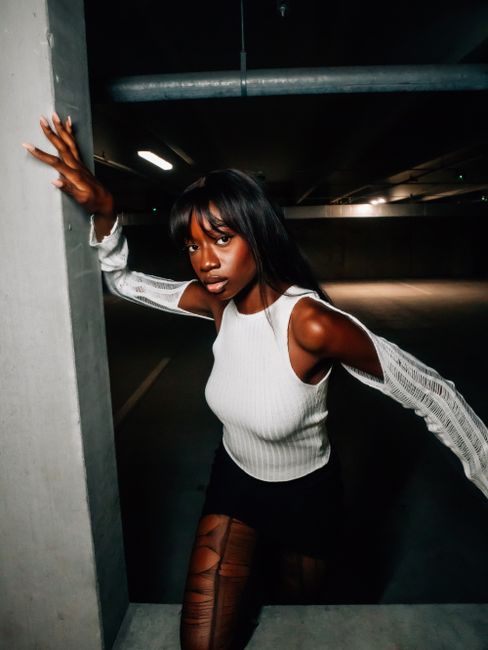 Dynamic editorial shot of a stylish woman posing dramatically in an urban parking garage.