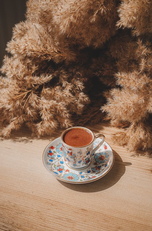 Porcelain Coffee Cup and a Saucer Standing on a Table Decorated with Dried Plants