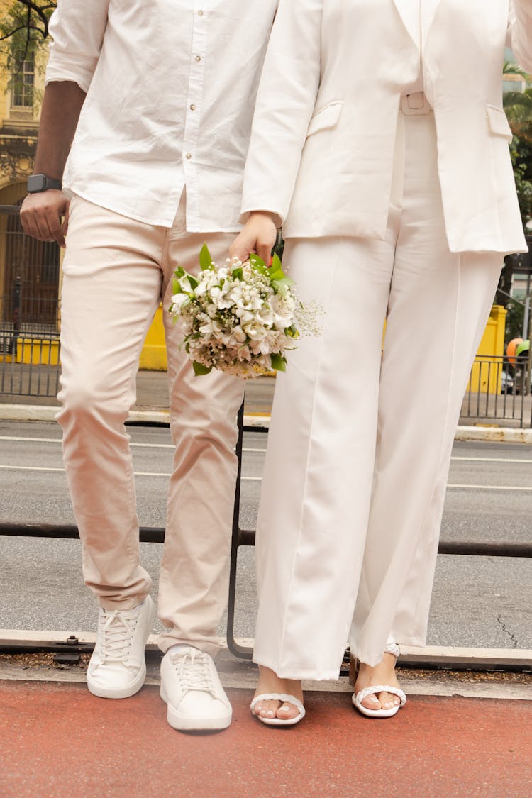 Elegant Couple In White Clothes Standing Outside And Woman Holding A Bouquet 