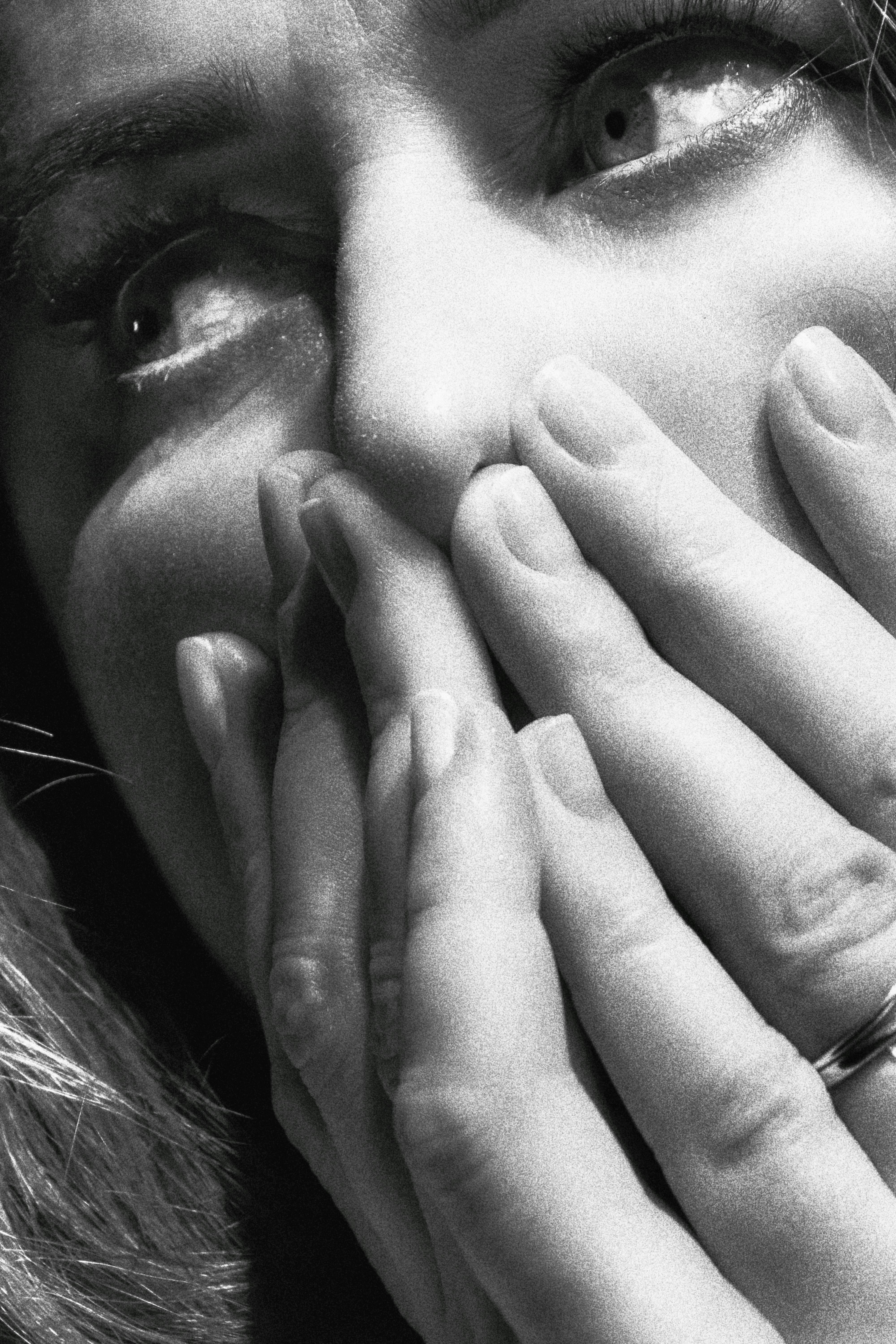 Close-up black and white portrait of a surprised woman covering her mouth with hands, expressing emotion.