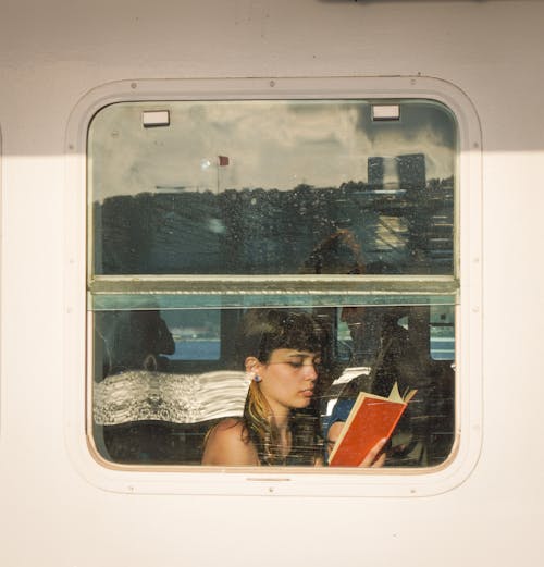 Woman Sitting by the Window in a Ferry and Reading a Book 
