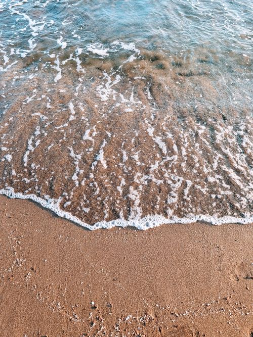 Free Gentle waves washing over golden sand on a tranquil beach during daylight. Stock Photo