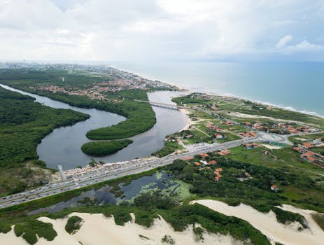 Aerial shot of Fortaleza's lush coastline, featuring winding river, dunes, and ocean.
