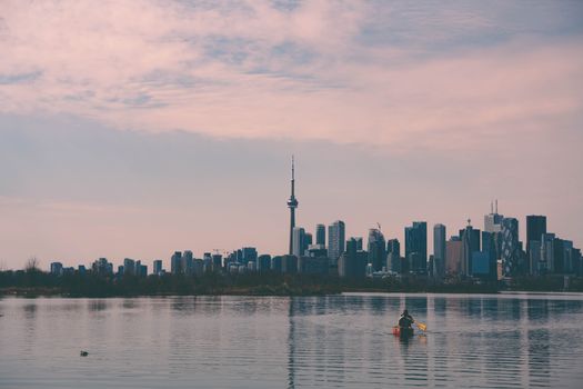 Serene lakeside view of Toronto skyline with a canoe on the water under a cloudy sky.