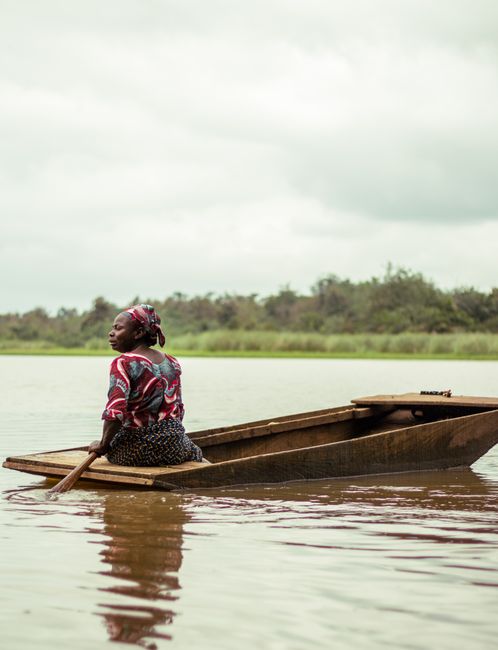 A woman paddles a wooden boat in a serene setting, emphasizing tranquility and culture.