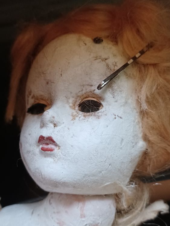 Boneca da Ilha das Bonecas Rosto de boneca antiga e deteriorada com olhos vazios e pintura descascada, representando as bonecas macabras da Ilha das Bonecas no México