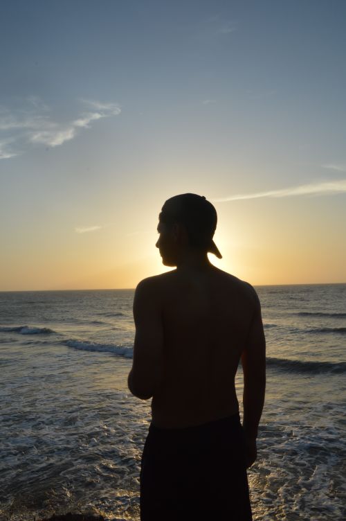 Free Silhouette of a man wearing a cap, standing at the seashore during sunset. Stock Photo