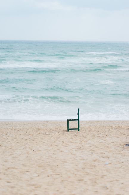 A lone green chair on the sandy beach of Nha Trang, Vietnam, facing the ocean waves.