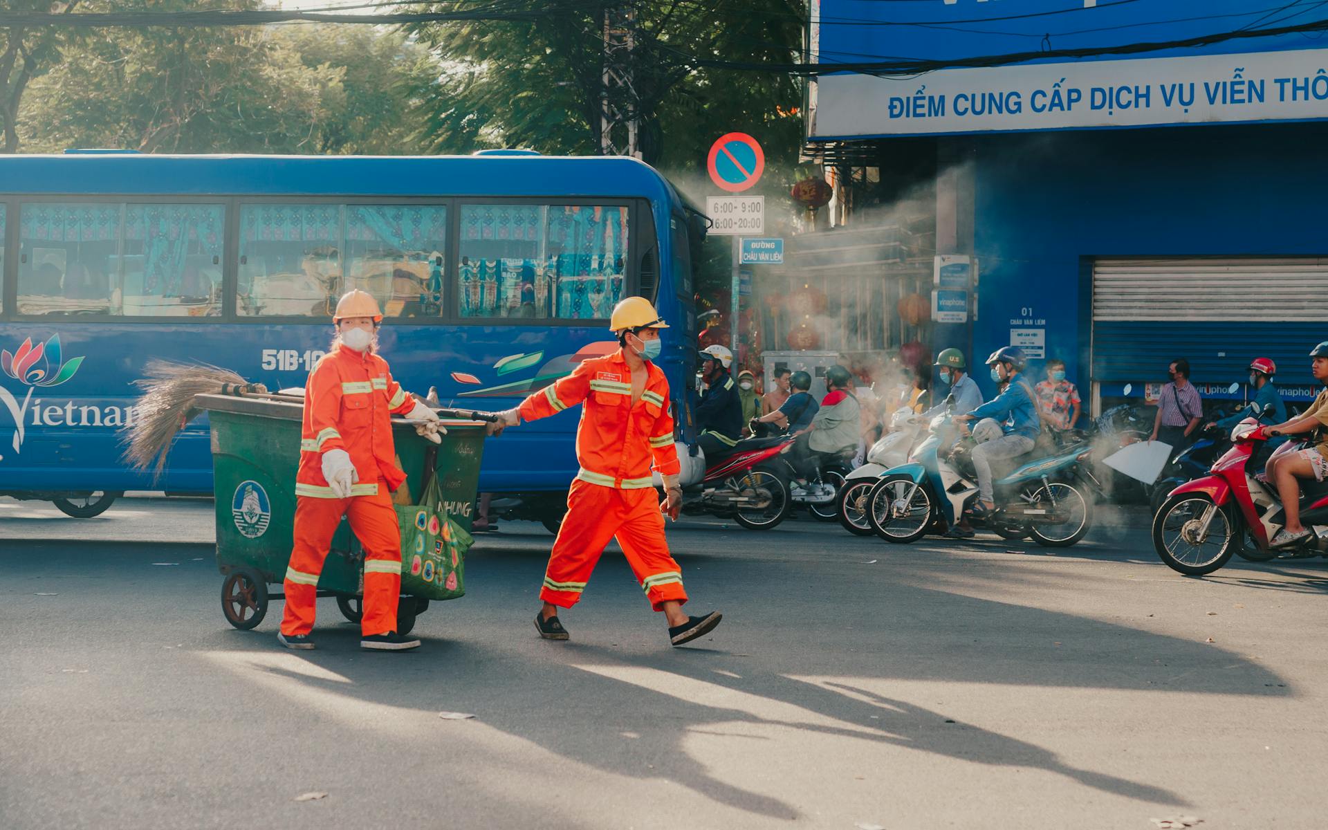 Sanitation workers collecting trash on bustling Ho Chi Minh City streets with traffic around.