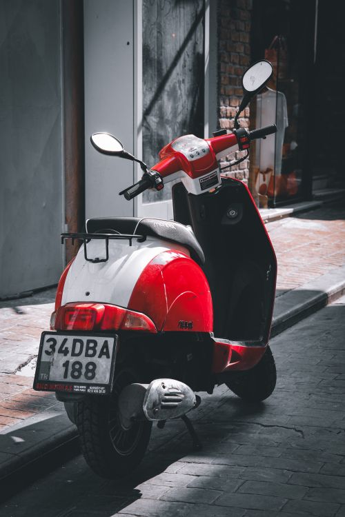 Free Parked red and white motor scooter on a sunlit urban street showcasing city life. Stock Photo