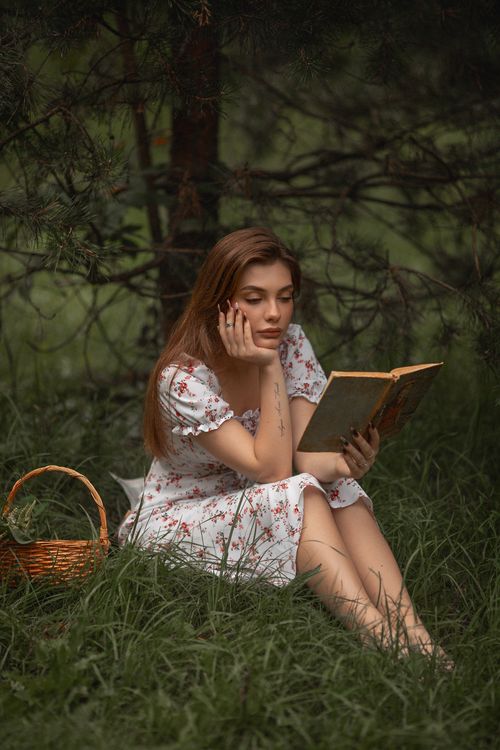 Free Young woman in a floral dress reading a book in a serene forest setting during summer. Stock Photo