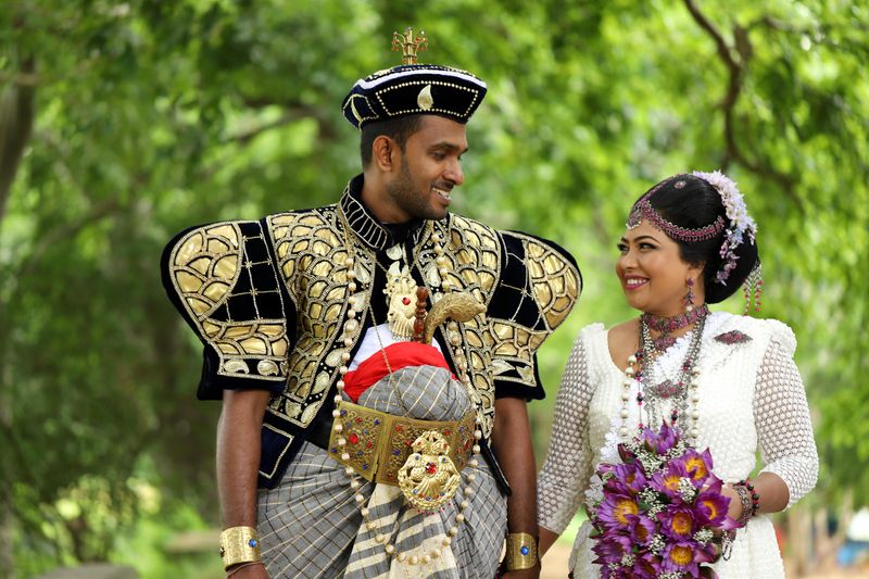 Sri Lankan couple in traditional wedding attire amidst lush green backdrop