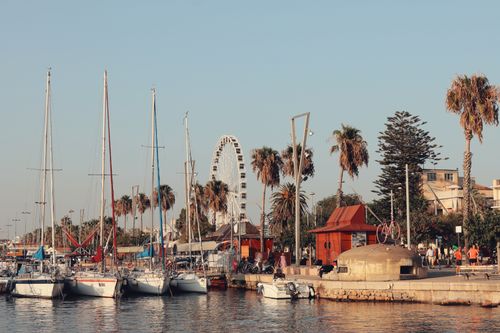 Free Explore the picturesque harbor of Alghero, Sardinia with sailboats and palm-lined promenade. Stock Photo