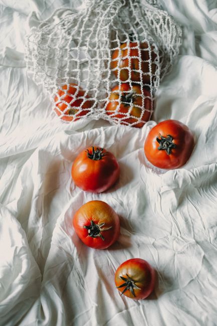 Top view of ripe organic tomatoes in a net bag on white fabric, emphasizing natural freshness.