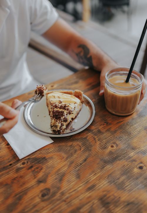 Free A close-up of a man with tattoos enjoying cheesecake and iced coffee at a café. Stock Photo