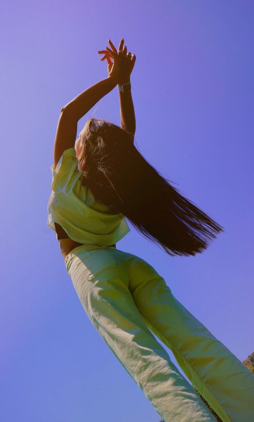 Free An artistic photo of a woman posing elegantly in yellow clothes against a vibrant blue sky. Stock Photo