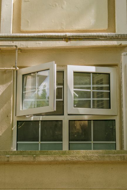 Photo by Maxine Xin on Pexels A tilted open window on a beige urban building facade with sunlight and shadows.