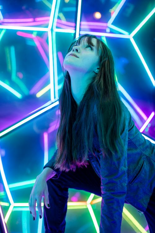 Free Young woman in a vibrant LED-lit geometric room posing with a futuristic vibe. Stock Photo