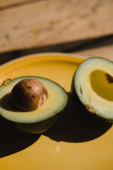 Sliced avocado on a vibrant yellow plate, showcasing summer colors and textures.