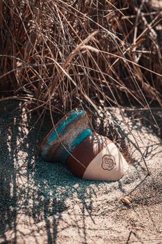 A rustic pot partially buried in sandy beach under dry grass, evoking tranquility.