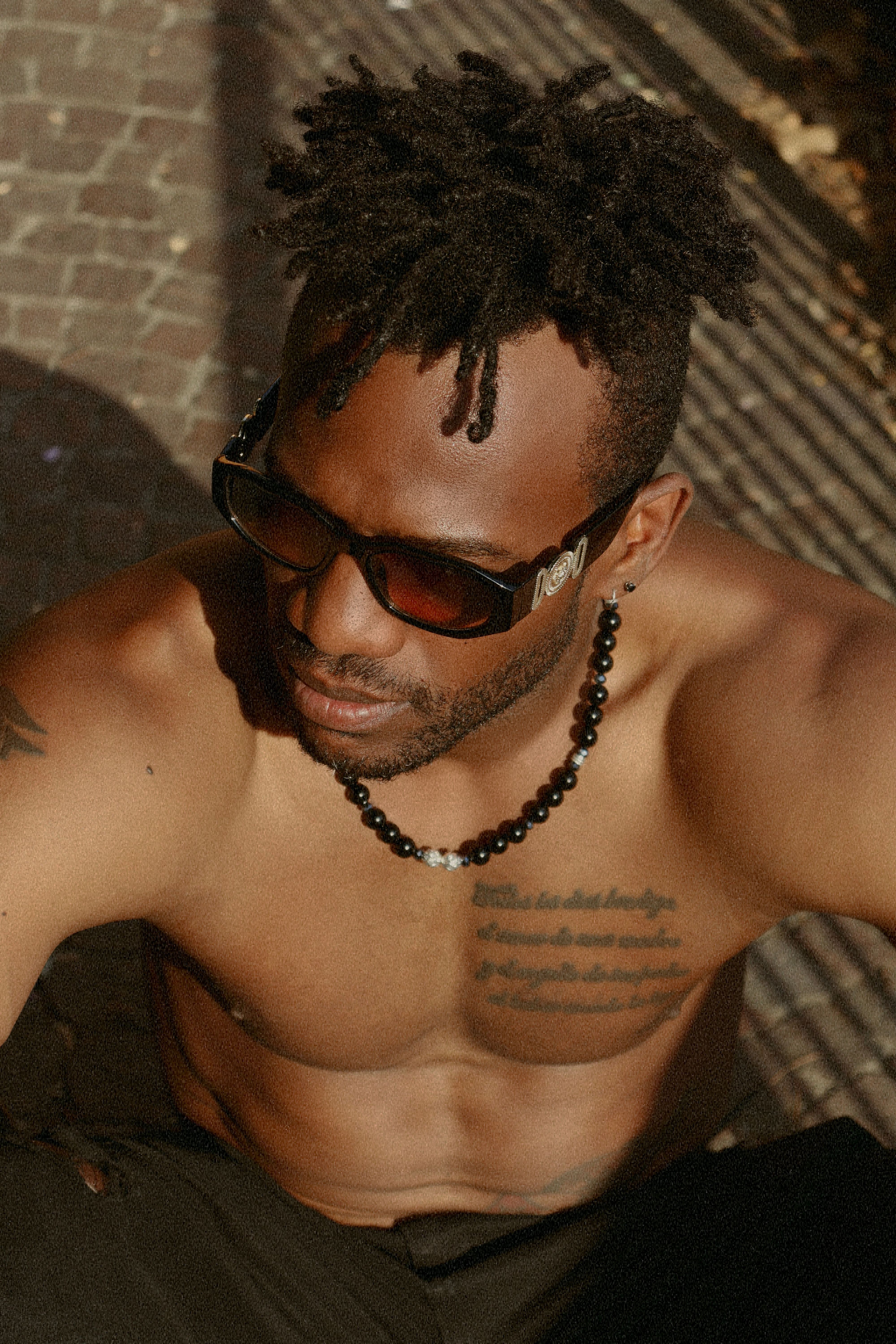 Muscular man with tattoos and sunglasses sitting outdoors in San Giovanni in Persiceto, Italy.