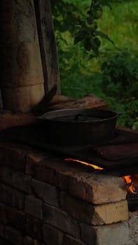 A rustic scene of a pot cooking on a traditional outdoor brick stove in a natural setting.