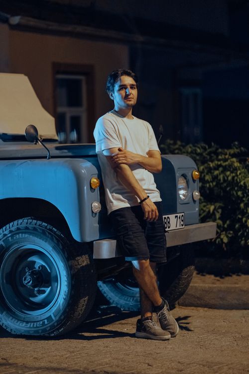 Free Man leans casually against a blue truck in an urban setting at night. Stock Photo