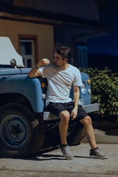 Young man sitting relaxed against a classic blue truck during an evening in summer.