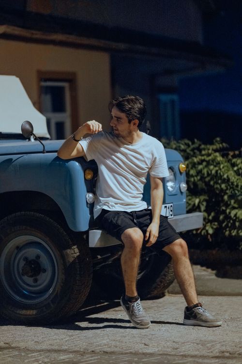 Free Young man sitting relaxed against a classic blue truck during an evening in summer. Stock Photo