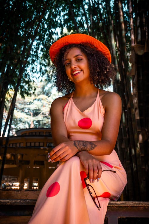 Woman in Pink Dress and Red Hat Sitting on Bench in Shade