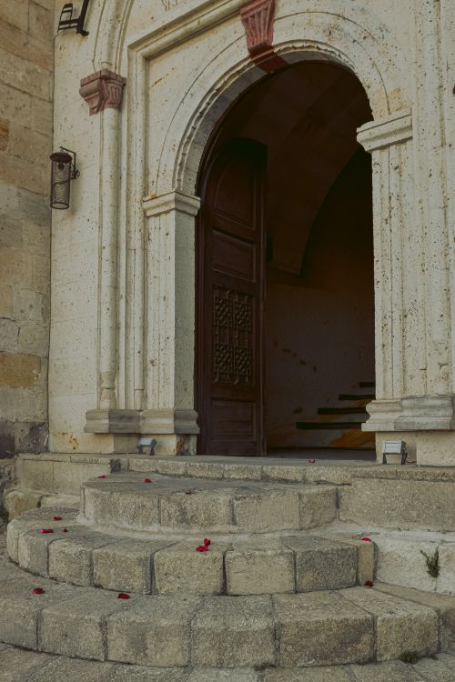 Free A classic arched stone entrance with wooden doors and scattered rose petals on steps. Stock Photo
