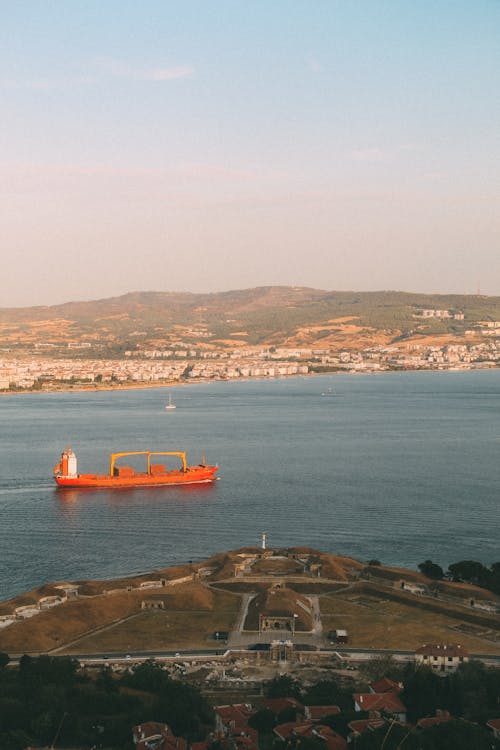 Cargo Ship Sailing on River with Town behind