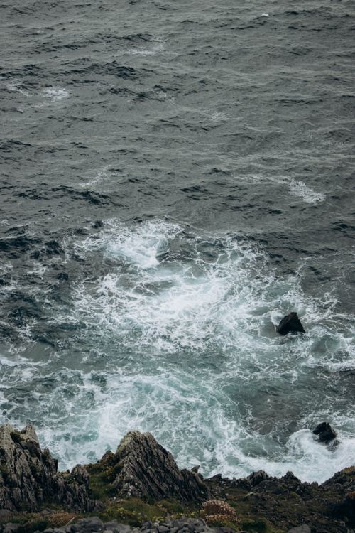 Free A high-angle view of powerful waves crashing against a rugged rocky coastline, creating dramatic splashes. Stock Photo