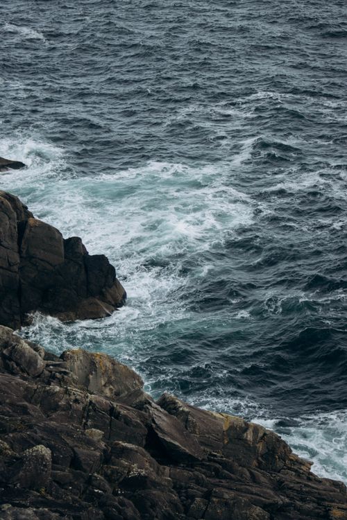 Free Dramatic view of a rocky coastline with ocean waves crashing into the shore, perfect for sea and adventure themes. Stock Photo