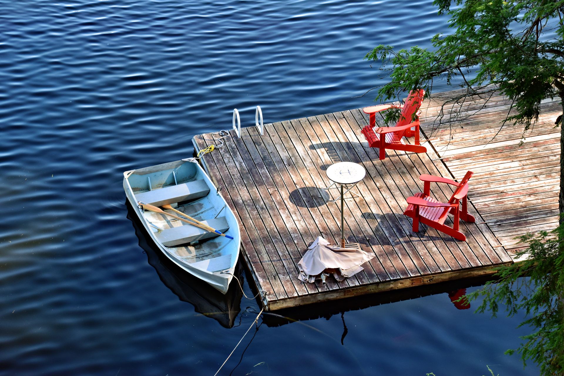 Tranquil scene of a wooden pier with red chairs and a rowboat on a calm lake, perfect for relaxation.