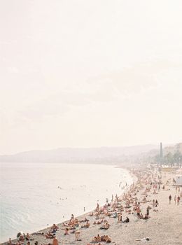 Crowded beach scene in Nice, France with sunbathers enjoying the sun and sea.